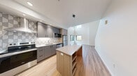 Located at 435 Alexander Loop in Eugene, Oregon, this contemporary two-story home offers three bedrooms and two bathrooms across two well-proportioned floors. The main level immediately impresses with its soaring double-height ceilings and light-toned hardwood-style flooring that flows throughout the open living area. Large windows at multiple levels flood the space with natural light and frame views of the surrounding greenery. A wall-mounted mini-split system provides efficient climate control.

The kitchen is a standout feature, outfitted with sleek gray cabinetry, a geometric patterned tile backsplash, stainless steel appliances, and a generously sized island with built-in shelving — ideal for both cooking and casual dining. Pendant lighting adds a modern finishing touch overhead.

Upstairs, the spacious primary bedroom offers plush carpeting, a large window with outdoor views, and comfortable proportions. Additional bedrooms share the soft carpet finish and clean, neutral palette. Both bathrooms are thoughtfully designed with warm wood-toned vanities, white quartz countertops, oval mirrors, and accessibility-friendly grab bars. The upper hallway conveniently houses a stacked in-unit washer and dryer. Throughout, the home reflects a clean, modern aesthetic with quality finishes and functional design.