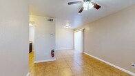 This single-floor unit is designed with a practical, open layout that maximizes usability across its living spaces. The main living area is finished with large-format tile flooring in a warm tan tone, contributing to a clean and cohesive aesthetic. A ceiling fan with integrated lighting provides both air circulation and ambient illumination, while a sliding door dressed with vertical blinds allows natural light to filter in. A centrally mounted thermostat and overhead HVAC vents indicate a dedicated climate control system throughout.

The kitchen is configured with a peninsula-style pass-through counter featuring a light-toned laminate surface and an integrated sink. Dark espresso cabinetry lines the walls, providing substantial storage, while white appliances — including a freestanding range and refrigerator — complete the functional setup. An overhead exhaust hood is positioned above the stove, and flush ceiling lighting keeps the kitchen well-lit.

The bedrooms are carpeted and offer a softer, quieter feel compared to the tiled common areas. Each room is equipped with a ceiling fan and features dual reach-in closets with built-in hanging rods and shelving, offering generous storage capacity. A walk-in closet is also present in at least one bedroom, further enhancing storage options throughout the unit.
