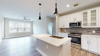 This well-appointed 3-bedroom, 2-bathroom residence in Frederick, MD offers a thoughtfully designed single-floor layout with modern finishes throughout. The open-concept kitchen and living area serves as the heart of the home, anchored by a large central island with a white quartz countertop, a deep undermount sink with a brushed gold faucet, and stylish pendant lighting. The kitchen is fully equipped with stainless steel appliances — including a gas range, built-in microwave, French door refrigerator, and dishwasher — complemented by crisp white shaker cabinetry, glass-front upper cabinets, and a textured gray tile backsplash. Wood-look flooring runs consistently throughout the unit, adding warmth and continuity. The living area features a ceiling fan and natural light from large windows with blinds. Each of the three bedrooms is generously sized, with the primary bedroom offering ample space, a ceiling fan, and a closet. Both bathrooms are finished with white shaker vanities, quartz countertops, brushed nickel hardware, and tile-surround shower and tub combinations. The neutral color palette and clean design create a bright, cohesive ambiance throughout this modern Frederick home.