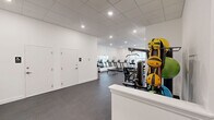 Located at 268 Market St in South Burlington, Vermont, this fitness center offers a thoughtfully designed exercise room spread across a single floor. The space features clean white walls, a drop-panel ceiling with recessed lighting, and durable dark rubber flooring suited for high-traffic athletic use.

The room is comprehensively equipped to support a wide range of workout styles. Cardio options include multiple treadmills and stationary cycling bikes with digital displays. For strength training, the space provides a selection of selectorized machines for targeted muscle groups, a multi-function cable station, a rack of dumbbells spanning various weights, and a flat workout bench. A dedicated functional training area along one wall is stocked with medicine balls, stability balls in multiple sizes, resistance accessories, and exercise mats organized neatly on storage racks.

A wall-mounted split air conditioning unit ensures climate control throughout the room, while a baseboard heater along one wall provides supplemental heating during Vermont's colder months. A large wall mirror enhances the sense of openness and allows users to monitor their form. Natural light filters in through a window, adding brightness to the well-lit interior. Storage lockers are also available within the space. The overall layout is open and organized, providing ample room to move freely between equipment stations.