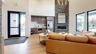 Located on E Prehistoric Dr in Pleasant Grove, Utah, this thoughtfully designed single-floor living space makes a striking first impression with its dramatic soaring ceilings that amplify the sense of openness. The living room serves as the heart of the space, anchored by a floor-to-ceiling stacked stone accent wall housing a sleek linear fireplace — a standout architectural feature that adds both warmth and texture.

Light hardwood flooring runs throughout, complementing the bright, neutral color palette of the crisp white walls. Abundant natural light pours in through a generous arrangement of large, black-framed windows, with clerestory windows positioned high on the walls to further enhance the airy atmosphere. An exposed HVAC duct adds an industrial design touch overhead, balanced by an elegant geometric chandelier that provides refined contrast.

A compact kitchenette is neatly integrated along one wall, featuring dark wood cabinetry, light countertops, a stainless steel refrigerator, and a microwave — offering practical functionality within the open-plan layout. Decorative frosted glass panels with intricate patterning serve as a distinctive interior design element along one wall. A corridor visible from the main area leads to an adjacent office space, suggesting the versatility of the overall floor plan.