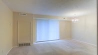 This single-floor residence offers a welcoming and functional layout designed for comfortable everyday living. The main living and dining area is an open, generously proportioned space anchored by soft, plush wall-to-wall carpeting that adds warmth underfoot. A large picture window fitted with vertical blinds serves as the focal point of the room, allowing natural light to filter in and brighten the neutral, warm-toned walls. An elegant chandelier overhead adds a refined touch to the dining area, creating a subtle distinction between the living and dining zones. The textured ceiling provides additional visual character throughout the space. Practical features include multiple HVAC vents integrated into both the ceiling and walls, ensuring year-round climate control. The overall ambiance is clean, airy, and move-in ready, with a simple and classic interior palette that provides a neutral canvas for a variety of décor styles. The single-floor layout promotes ease of movement and accessibility throughout the home, making it a practical and inviting space suited for a range of lifestyles.