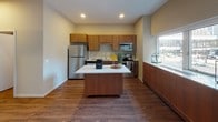 This single-floor space is designed with a cohesive, modern aesthetic, combining functional layouts with warm, contemporary finishes. The kitchen serves as a central highlight, featuring a full suite of stainless steel appliances including a refrigerator, electric range, built-in microwave, and dishwasher. Rich, medium-toned wood cabinetry provides ample storage, while light countertops offer generous prep space. A central island adds additional workspace and a natural gathering point. A large window allows natural light to fill the kitchen, enhancing the open, airy feel of the area.

The bedroom area is spacious and uncluttered, with warm wood-look flooring that carries throughout the unit, neutral wall tones, and a standard interior door providing closet or utility access. The ceiling-mounted light fixture and visible HVAC vent reflect practical, well-planned infrastructure.

The bathroom is laid out efficiently in a galley style, featuring a floating vanity with dark wood cabinetry and a white countertop, a standard toilet, and wood-look flooring consistent with the rest of the unit. Chrome towel bars and clean wall finishes complete the space with a polished, functional look.