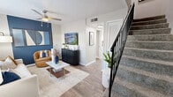 Located in Hattiesburg, Mississippi, this two-story, 2-bedroom, 2-bathroom home offers a thoughtfully designed layout spread evenly across two floors. The main level features an open-concept living, dining, and kitchen area highlighted by warm wood-look flooring and bold blue accent walls that lend a modern, cohesive aesthetic. The living room benefits from large windows that invite natural light and features a ceiling fan, while a carpeted staircase with a sleek black railing connects to the upper level. The kitchen is well-appointed with white shaker-style cabinetry, granite countertops, stainless steel appliances including a range, microwave, and dishwasher, and a skylight that further brightens the space. The adjacent dining area is defined by a striking blue accent wall and a window overlooking the exterior. Upstairs, the primary bedroom offers a generous footprint with plush carpet, natural light from a large window with decorative curtains, and a ceiling fan. The second bedroom mirrors the contemporary styling with a dark accent wall and ceiling fan. Two full bathrooms complete the home, finished in neutral tones. Throughout, textured ceilings and consistent design details create a polished, move-in-ready living environment.