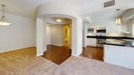 This single-floor residence showcases a thoughtfully designed layout with a blend of architectural character and functional living spaces. The entryway immediately impresses with a dramatic circular rotunda ceiling accented by a warm tray detail and a central flush-mount light fixture. Curved walls with built-in display niches frame a transition from rich hardwood flooring into the carpeted living areas beyond, where sliding glass doors fitted with vertical blinds invite natural light and outdoor views.

The living spaces are generously proportioned, featuring neutral-toned carpet, clean white walls, and additional sliding glass door access. A dedicated bedroom offers a tray ceiling, a wide window with outdoor views, plush carpet, and a built-in closet. A second carpeted room provides comparable scale and natural light through its own glass door.

The kitchen is equipped with white cabinetry, dark granite countertops, open shelving, stainless steel appliances including a range, microwave, and dishwasher, and a double-basin sink beneath a bright window. A graceful arched passageway connects the kitchen corridor to the main living areas.

Two bathrooms serve the residence. One features white cabinetry, a vessel sink, dark granite counters, a soaking tub, and subway tile surround. The second offers a glass-enclosed shower, soaking tub, subway tile walls, and tile flooring with a dark granite accent bench.