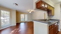 This single-floor residence offers a thoughtfully designed layout that balances open communal spaces with comfortable private areas. The living and dining area is anchored by rich hardwood flooring, crown molding, and a ceiling fan, while multiple windows and a glass-paneled door allow generous natural light and views of the outdoors. The kitchen is connected to the living space via a pass-through breakfast bar, and features warm wood cabinetry, granite-style countertops, a stainless steel refrigerator, and an electric cooktop. A convenient in-unit laundry area is accessible directly from the kitchen. The bedrooms are generously sized, each finished with plush carpet, crown molding, ceiling fans, and windows that invite natural light. The primary bedroom includes an ensuite bathroom with wood cabinetry, while a second full bathroom serves the remaining rooms—both bathrooms are fitted with a tub-shower combination and classic white tile surrounds. Consistent warm neutral tones and clean white trim throughout the space create a cohesive, inviting atmosphere that is both functional and easy to personalize.