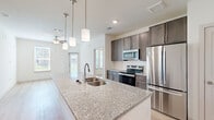 Located at 1200 Deer Moss Loop in Niceville, FL, this well-designed single-story home offers 2 bedrooms, 3 bathrooms, and two dedicated closets in a thoughtfully laid-out floor plan. The open-concept kitchen serves as the centerpiece of the home, showcasing a large granite-topped island with a double basin sink and elegant pendant lighting. Dark-toned cabinetry pairs with a white subway tile backsplash and a full suite of stainless steel appliances, including a refrigerator, microwave, and electric range. Light wood-look flooring flows through the kitchen and living areas, complemented by ceiling fans that enhance airflow and comfort. The primary bedroom features light wood flooring and access to a private en-suite bathroom, which includes a dark wood vanity with granite countertop, a glass-enclosed shower, and light hardwood floors. A second bathroom offers a soaking tub surrounded by large-format neutral tile. The secondary bedroom is carpeted and bright, with dual windows allowing natural light and neighborhood views. Both closets provide practical wire shelving for ample storage. The home's clean, neutral palette and modern finishes create a cohesive, move-in-ready atmosphere throughout.