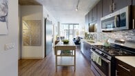 Located at 10 S Green St in Chicago's vibrant West Loop neighborhood, this single-floor unit blends industrial character with contemporary finishes. Exposed concrete ceilings run throughout, lending an urban loft aesthetic that defines the overall ambiance.

The kitchen is a functional highlight, outfitted with dark espresso cabinetry, stainless steel appliances including a gas range, microwave, refrigerator, and dishwasher, complemented by a mosaic tile backsplash and light quartz countertops. A freestanding island provides additional prep and dining space. A sliding barn door connects the kitchen to the open living area, which is bathed in natural light from expansive floor-to-ceiling windows offering views of the surrounding cityscape and greenery below.

The bedroom continues the industrial-modern aesthetic with the same soaring concrete ceiling, exposed structural columns, and generous windows that frame outdoor views, creating a bright and airy retreat. The full bathroom features a dark-framed vanity mirror, rich espresso cabinetry, a white quartz countertop, and a tiled tub-shower combination, providing a clean and polished finish. Hardwood-style flooring flows consistently throughout the living and kitchen areas, tying the space together cohesively.