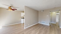Located at 1000 Pine Ave in Redlands, California, this well-appointed one-bedroom unit offers a thoughtfully designed single-level layout. The open-concept living room and kitchen area is anchored by light wood-look flooring that runs throughout, neutral warm-toned walls, and a textured ceiling. A ceiling fan adds comfort to the living space, while large windows fitted with vertical blinds and a sliding glass door to a private balcony invite generous natural light and outdoor views. The galley-style kitchen is efficiently arranged with ample white cabinetry, granite-look countertops along both sides, and black appliances including a gas range, refrigerator, and dishwasher, all illuminated by overhead lighting. A hallway connects the main living area to the bedroom, which features plush carpeting, a large window overlooking the surrounding neighborhood, and a full-width mirrored sliding closet that enhances the sense of space. The bedroom is notably generous in size, offering plenty of room for furniture arrangement. Throughout the unit, clean white baseboards, HVAC vents, and a consistent neutral color palette create a cohesive, move-in-ready atmosphere suited for comfortable everyday living.