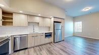This well-appointed one-bedroom, one-bathroom unit at 1905 Vine St in Kansas City, MO offers a thoughtfully designed layout across a single floor. The open-concept kitchen is a standout feature, showcasing light wood cabinetry, white subway tile backsplash, white quartz countertops, and a full suite of stainless steel appliances including a range, dishwasher, built-in microwave, and refrigerator. Recessed lighting illuminates the kitchen, which flows seamlessly into the living area. The living room features wood-look luxury vinyl plank flooring, neutral walls, and a private entry door with a sidelight window, as well as an additional window for natural light. The bedroom is carpeted for comfort and includes a window with natural light and direct access to a spacious walk-in closet outfitted with wire shelving and hanging rods. In-unit stacked laundry is conveniently accessible from the bedroom area. The bathroom features a walk-in shower, wood-toned vanity, and clean white tile accents. Throughout the unit, a cohesive palette of warm neutrals and modern finishes creates a clean, contemporary ambiance.