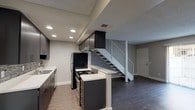 This two-story residence offers a well-organized layout across two distinct levels, combining modern updates with comfortable living spaces. The main level features an open-concept living and dining area finished with dark hardwood-style flooring that extends throughout. A sliding glass door floods the living space with natural light and provides access to an outdoor patio area. The kitchen is a standout feature, showcasing dark cabinetry, white countertops, a mosaic tile backsplash, stainless steel appliances including a refrigerator and range, recessed lighting, and a peninsula with additional counter space. A staircase with a metal railing connects the main level to the upper floor. The upper level is home to the bedrooms, each distinguished by their distinctive white-painted wood beam ceilings with tongue-and-groove paneling, lending a warm architectural character to the space. The bedrooms are finished with plush carpeting and feature generous built-in closet storage. Large windows allow ample natural light to filter in, offering views of surrounding greenery. A full bathroom on this level includes a shower-tub combination. Throughout the residence, neutral wall tones create a clean, cohesive aesthetic that complements both levels of the home.