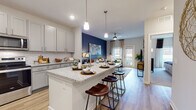 Located at 142 Patrick Murphy Dr in Morganton, NC, this thoughtfully designed single-floor residence offers a seamless blend of modern finishes and functional living spaces. The open-concept kitchen is a standout feature, boasting gray shaker-style cabinetry, granite countertops, a classic white subway tile backsplash, and a full suite of stainless steel appliances including a refrigerator, range, microwave, and dishwasher. A generously sized kitchen island with bar seating bridges the kitchen and living areas, making it ideal for entertaining. The living room is bathed in natural light from a sliding glass door that opens to a private balcony, and is complemented by light wood-style flooring and a ceiling fan. A bold navy accent wall adds a striking design element to the open living space. The bedroom is a serene retreat featuring plush carpeting, a dramatic dark accent wall, a ceiling fan, and ample natural light from large windows with blinds and curtains. The full bathroom is finished with granite countertops, wood-style flooring, and a soaking tub with a tile surround. A dedicated in-unit laundry room with side-by-side washer and dryer and overhead shelving completes this well-equipped residence.