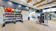 Located at 5905 Campbellton Rd SW in South Fulton, GA, this fitness center offers a thoughtfully designed, single-floor layout that accommodates a wide range of workout styles. The space features striking navy blue accent walls paired with crisp white wainscoting, creating a bold yet clean aesthetic throughout. Rustic wooden beam accents line the coffered ceiling, complemented by recessed lighting and large ceiling fans that enhance airflow and comfort during workouts.

The facility is organized into distinct training zones. The strength and functional training area is stocked with a comprehensive selection of kettlebells, medicine balls, stability balls, TRX suspension trainers, and resistance equipment neatly arranged on multi-tier storage racks. A cable and selectorized weight machine station provides additional resistance training options. The cardio zone includes ellipticals, treadmills, and stationary spin bikes equipped with individual screens.

A dedicated studio area benefits from floor-to-ceiling windows along multiple walls, flooding the space with abundant natural light and offering views of the outdoor pool area. Carpet tile flooring in a herringbone pattern runs throughout, providing traction and comfort underfoot. Wall-mounted televisions and full-length mirrors further enhance the training environment, making this fitness center a well-rounded and inviting space for residents.