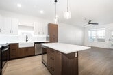 This well-appointed one-bedroom, one-bathroom unit offers a thoughtfully designed layout across a single floor, making efficient use of every square foot. The open-concept kitchen is a standout feature, showcasing a two-tone cabinetry scheme that pairs white upper cabinets with warm wood-toned lower cabinets, illuminated by under-cabinet LED lighting. A central island with a quartz countertop and pendant lighting overhead anchors the space, while stainless steel appliances—including a refrigerator, range, microwave, and dishwasher—add a polished, functional edge. A farmhouse-style sink completes the kitchen's contemporary aesthetic. Light wood-look flooring flows throughout the main living areas, extending into the bright living room, which features a ceiling fan, large windows, and a private exterior door that invites natural light and outdoor views. The bedroom is carpeted for comfort, fitted with its own ceiling fan, and receives natural light through a double-hung window. The bathroom is finished with a glass-enclosed walk-in shower, wood-toned vanity, and matte black hardware accents. A dedicated in-unit laundry room with a full-size washer and dryer adds practical convenience.