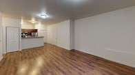 Located at 10436 SE Carr Rd in Renton, Washington, this single-story unit offers a practical and well-organized layout. The open-concept living and dining area is a standout feature, showcasing rich, dark hardwood-style flooring that runs throughout the main living spaces, contributing to a warm and cohesive aesthetic. Natural light enters through a large window fitted with vertical blinds, and a door provides direct exterior access, enhancing the sense of openness.

The kitchen is positioned adjacent to the living area and is defined by a peninsula-style breakfast bar that serves as a natural divider. Warm-toned wood cabinetry pairs with stainless steel appliances, including a refrigerator, gas range, and microwave, creating a functional cooking space. A double-door closet near the kitchen entry offers convenient storage.

The bedrooms are carpeted for comfort and feature clean white walls and ample closet space with paneled double doors. One room includes a wall-mounted electrical panel. Both rooms are well-proportioned and receive natural light through windows. The unit's neutral color palette and consistent design elements throughout provide a clean, move-in ready environment suited to a variety of living arrangements.