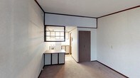 This single-floor space presents a straightforward, functional layout that combines the living and kitchen areas within a cohesive open-concept design. The living area is finished with wall-to-wall carpeting in a neutral tone, providing a practical foundation, while dark baseboards and trim work create a defined contrast against the light-colored walls throughout.

A distinctive interior pass-through window connects the main living space to the kitchen, framed in dark trim that echoes the room's overall aesthetic. The kitchen is equipped with a white range and oven, overhead cabinetry, and a countertop with sink, offering efficient use of the available space. A peninsula-style counter extends into the main living area, functioning as a divider while also providing additional workspace or casual dining potential.

A dark wood-toned door is positioned along one wall, leading to an adjacent area. The ceilings are standard height with a clean, flat finish, and recessed lighting in the kitchen ensures adequate illumination. Overall, the space maintains a utilitarian character with a clean, minimal aesthetic suited for practical everyday living.
