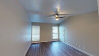 This single-floor unit offers a clean, functional layout designed for comfortable everyday living. The main living area is bright and open, featuring durable wood-look plank flooring, neutral-toned walls, and a ceiling fan with integrated lighting. Two windows dressed with horizontal blinds allow natural light to fill the space while maintaining privacy. The living area flows seamlessly into the kitchen, which is defined by a peninsula counter with a dark countertop surface, white upper cabinetry, and stainless steel appliances including a refrigerator and range. Adjacent to the kitchen, a dedicated laundry area provides added convenience. The bedroom continues the wood-look flooring and offers a window with blinds, creating a calm and functional retreat. A ceiling fan is also present in this room. The full bathroom is well-appointed with a white vanity featuring a single undermount sink, dark countertop, a framed mirror, and a well-lit vanity bar above. A combined tub and shower with a rainfall-style showerhead completes the space. Throughout, textured popcorn ceilings and clean white baseboards contribute to a consistent and practical interior aesthetic.
