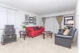 Located in West Bloomfield, Michigan, this single-floor residence offers a well-organized layout designed for comfortable everyday living. The generously sized living room serves as the heart of the home, featuring plush wall-to-wall carpeting, large windows with vertical blinds that invite abundant natural light, and ample space for relaxed seating arrangements. Framed artwork adorns the walls, adding a curated, lived-in character to the space. Adjacent to the living area, the dining space is thoughtfully arranged with both a formal dining set beneath a pendant light fixture and a smaller bistro-style table, offering flexible options for entertaining or casual meals. The kitchen is outfitted with dark espresso cabinetry, dark granite-style countertops, a decorative tile backsplash, and a full suite of stainless steel appliances including a range, microwave, and dishwasher — combining style with practicality. A cozy study nook provides a quiet retreat, complete with a classic wooden desk, natural window light, and carpeted flooring. The bathroom makes a bold statement with vibrant red walls, dark wood vanity cabinetry, granite countertops, a framed mirror, and tile flooring, creating a striking and memorable interior accent throughout the home.