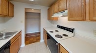 This single-floor residence offers a clean, well-maintained layout with a consistent design language throughout. The most striking feature is the warm, honey-toned parquet wood flooring that extends across the living areas and bedroom, adding a classic character to each room.

The spacious living area is bathed in natural light, with large windows casting patterned light across the polished floors. A full-width sliding glass door fitted with vertical blinds opens to an outdoor area, further brightening the space and providing a seamless indoor-outdoor connection. A secondary window nearby adds additional ventilation and light.

The bedroom is generously proportioned, featuring the same parquet flooring and a large window with a view of the exterior. Ample built-in closet space, including a walk-in style storage area adjacent to the room, ensures practical storage solutions.

The kitchen is equipped with warm oak cabinetry, an electric coil range with overhead ventilation, and light-toned countertops. A dedicated storage closet adjacent to the kitchen provides additional utility. Light tile flooring grounds the kitchen area practically.

The bathroom features a full soaking tub and shower combination, accented by clean light-blue square tile surround and a chrome grab bar, complemented by bright white fixtures throughout. The overall ambiance of the space is bright, tidy, and functional, with a timeless residential aesthetic.
