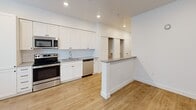 Located at 1925 W North Temple in Salt Lake City, UT, this one-bedroom, one-bathroom unit offers a thoughtfully designed single-floor layout that makes excellent use of its compact footprint. Light wood-style flooring runs consistently throughout, lending a warm, cohesive feel to the entire space.

The open-concept living, dining, and kitchen area serves as the heart of the unit. The kitchen is outfitted with crisp white shaker cabinetry extending to the ceiling, a classic white subway tile backsplash, gray countertops, and a full suite of stainless steel appliances including a refrigerator, range, over-the-range microwave, and dishwasher. A peninsula with a raised countertop provides a natural division between the kitchen and the living area, ideal for casual dining or meal prep. Large windows flood the main living space with natural light.

The bedroom is a bright, serene retreat featuring a wide bank of windows with blinds that allow for ample natural light and privacy. Recessed lighting adds to the clean, modern aesthetic.

The bathroom presents a clean, all-white design with a soaking tub and shower combination, tiled surround with built-in shelving, a white vanity with dark hardware, and gray countertops. The unit also includes two closets, an in-unit laundry area, and a hallway connecting the private rooms — delivering practical, well-organized living.