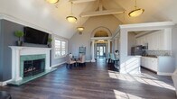 Located at 2223 Craigside Dr in Columbus, Ohio, this single-floor community clubhouse is designed with a refined architectural style and a welcoming, open layout. The interior is unified by rich dark hardwood flooring that runs throughout, complemented by soft gray walls and crisp white trim.

The grand entryway greets visitors with a striking arched transom, decorative columns, and pendant lighting that draws the eye upward toward soaring vaulted ceilings. This architectural centerpiece sets the tone for the elegance found throughout the space.

The main gathering area is divided into two distinct zones. A lounge area features a marble-surround fireplace with a green stone hearth, a wall-mounted television, and comfortable seating bathed in natural light from large multi-pane windows. An arched window near the roofline adds additional brightness and character. Direct access to an outdoor pool area is provided through a glass door in this room.

Adjacent to the lounge, a dining area offers a round glass-top table surrounded by upholstered chairs, positioned beside a decorative ladder shelf and large windows overlooking the exterior greenery.

The galley kitchen is well-appointed with white cabinetry, granite countertops, a mosaic tile backsplash, stainless steel appliances, and a double basin sink — providing full functionality for gatherings and events.