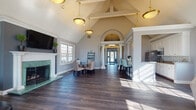Located at 2223 Craigside Dr in Columbus, Ohio, this single-floor community clubhouse is designed with a refined architectural style and a welcoming, open layout. The interior is unified by rich dark hardwood flooring that runs throughout, complemented by soft gray walls and crisp white trim.

The grand entryway greets visitors with a striking arched transom, decorative columns, and pendant lighting that draws the eye upward toward soaring vaulted ceilings. This architectural centerpiece sets the tone for the elegance found throughout the space.

The main gathering area is divided into two distinct zones. A lounge area features a marble-surround fireplace with a green stone hearth, a wall-mounted television, and comfortable seating bathed in natural light from large multi-pane windows. An arched window near the roofline adds additional brightness and character. Direct access to an outdoor pool area is provided through a glass door in this room.

Adjacent to the lounge, a dining area offers a round glass-top table surrounded by upholstered chairs, positioned beside a decorative ladder shelf and large windows overlooking the exterior greenery.

The galley kitchen is well-appointed with white cabinetry, granite countertops, a mosaic tile backsplash, stainless steel appliances, and a double basin sink — providing full functionality for gatherings and events.