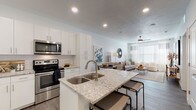 This single-story residence presents a thoughtfully designed open-concept layout that seamlessly connects the kitchen and living areas. The kitchen serves as a central focal point, showcasing white shaker-style cabinetry extending to the ceiling for ample storage, a white subway tile backsplash, and light granite countertops. A peninsula island with a double undermount sink and bar seating provides both additional workspace and a natural divider between the kitchen and living space. Stainless steel appliances, including a refrigerator, range, microwave, and dishwasher, complete the kitchen's modern aesthetic. Wood-style plank flooring runs throughout the main living areas, adding warmth and durability.

The living room receives natural light through large windows dressed with layered blinds and curtains, while a ceiling fan adds comfort. The bedroom continues the clean, neutral palette with its own ceiling fan, a window with natural light, and direct access to the bathroom. The bathroom features a white vanity with granite countertops, a large mirror, and wood-style flooring consistent with the rest of the unit. Recessed lighting and a crisp white color scheme throughout contribute to a bright, contemporary ambiance.