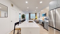 This thoughtfully designed one-bedroom, one-bathroom residence offers a contemporary open-concept floor plan that maximizes functionality and flow. Light-toned hardwood floors run throughout the main living areas, anchoring the modern aesthetic and creating a sense of continuity.

The kitchen serves as the centerpiece of the home, featuring a large white quartz waterfall island with an integrated sink and bar seating — ideal for casual dining or entertaining. Two-tone cabinetry pairs light wood upper cabinets with slate-gray lowers, complemented by a full suite of stainless steel appliances including a range, over-the-range microwave, dishwasher, and refrigerator.

The open living room receives ample natural light through oversized windows dressed with patterned drapes and roller shades, and includes direct access to a private patio. Recessed lighting throughout enhances the bright, airy ambiance.

The bedroom is a calm retreat, carpeted for comfort, with a large window, ceiling fan, and a dedicated closet. The bathroom features gray cabinetry, a white quartz vanity, and a clean, minimal design consistent with the rest of the home. A separate closet with built-in shelving provides additional storage, rounding out this efficient and well-appointed residence.