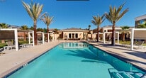 Located at 23742 Washington Avenue in Murrieta, California, this generously sized outdoor amenity space delivers a resort-style experience across a single-level layout. The centerpiece of the area is a large, sparkling rectangular swimming pool with vivid turquoise water, surrounded by a broad, open pool deck that provides ample room for lounging and recreation. Flanking the pool on both sides are rows of tall, mature palm trees that lend a tropical ambiance and provide natural shade throughout the day. A series of sleek, modern white pergola cabana structures are positioned along the pool perimeter, offering shaded seating areas ideal for relaxation. Additional lounge seating is distributed across the expansive deck, accommodating a large number of guests simultaneously. The surrounding multi-story residential buildings feature warm earth-toned stucco exteriors and wrap-around balconies that overlook the pool courtyard, creating an enclosed and cohesive community feel. A dedicated spa or wading area is visible at one end of the pool, adding further utility to the space. The overall design blends contemporary architectural elements with lush landscaping, benefiting from abundant natural sunlight characteristic of Southern California. The result is a vibrant, well-appointed outdoor retreat suited for both active use and quiet relaxation.