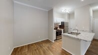This single-story unit in Greensboro, NC (27410) offers a well-organized layout with a cohesive neutral color palette of warm beige tones throughout. The open-concept living and kitchen area serves as the central hub of the space, featuring wood-look flooring, crown molding, and recessed lighting. The kitchen is equipped with white cabinetry, a tile backsplash, granite countertops, stainless steel appliances including a refrigerator and range, and a peninsula with a built-in sink that doubles as a breakfast bar. The living area benefits from a sliding glass door fitted with vertical blinds, allowing abundant natural light and outdoor access.

The bedrooms are carpeted and feature large windows with horizontal blinds that provide views of surrounding greenery. Several bedrooms include closets with paneled bifold doors, offering practical storage. One bedroom is conveniently positioned adjacent to a bathroom. The bathroom showcases wood-look flooring, a granite-topped vanity with white cabinetry, a framed mirror, and brushed nickel fixtures and grab bars. The textured ceilings are consistent throughout, and the overall layout, as visible in the 3D floor plan, is efficiently arranged to maximize usable living space.