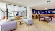 Located in the heart of Atlanta's vibrant Midtown district, this expansive single-floor amenity space at 391 17th St NW offers a thoughtfully designed environment for socializing, working, and relaxing. Light wood-tone flooring flows seamlessly throughout, unifying the various functional zones under bright, recessed lighting.

The open-plan living and lounge area features multiple seating arrangements, including plush sofas and accent chairs, anchored by a striking wood-paneled feature wall with a large mounted TV and built-in shelving. Floor-to-ceiling glass doors lead directly to an outdoor terrace, flooding the interior with natural light and offering views of an outdoor amenity area.

A bold navy blue accent wall with warm wood wainscoting defines the entertainment zone, which includes a billiards table, bar-height seating, and multiple screens. Adjacent to this is a glass-walled co-working room equipped with workstations, providing a quiet, focused environment.

The gourmet kitchen is a standout feature, showcasing warm wood cabinetry, a geometric patterned tile backsplash, stainless steel Viking appliances, a wine cooler, and a generous island with bar seating beneath pendant lighting. A secondary cabinetry wall with muted teal-toned storage adds further utility to the space. The overall ambiance is modern, inviting, and polished.