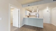 This single-floor residence offers a thoughtfully laid-out interior with a clean, contemporary aesthetic throughout. The open-concept kitchen is a standout feature, showcasing crisp white cabinetry, light quartz countertops, a peninsula with an undermount sink, and a full suite of stainless steel appliances including a range, over-the-range microwave, refrigerator, and dishwasher. Pendant lighting above the peninsula adds a polished finishing touch. The kitchen flows seamlessly into the living area, which is finished with durable wood-look flooring and features a sliding glass door with vertical blinds that opens to an outdoor balcony, filling the space with natural light. A secondary living or dining area offers additional flexibility with the same flooring and another sliding patio door. The bedrooms are carpeted for comfort, each featuring windows with horizontal blinds that allow for natural light and privacy. Two full bathrooms are appointed with dark espresso-toned vanities, white quartz countertops, large mirrors with bar lighting, and light tile flooring. One bathroom includes a shower-tub combo, while the other features an open, accessible layout. The overall palette of neutral tones, modern fixtures, and consistent finishes creates a cohesive and inviting living environment.