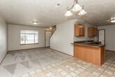 This two-story home is thoughtfully laid out across two levels, offering a functional and comfortable living environment. The main level presents an open-concept design where the kitchen flows seamlessly into the living and dining areas. The kitchen is well-equipped with warm wood cabinetry, dark countertops, tile flooring, and black appliances including a range, refrigerator, and built-in microwave. A peninsula with a sink serves as both a workspace and a visual divider between the kitchen and the adjacent carpeted living area. The living space is bright, benefiting from a large front-facing window that draws in natural light, and features a textured ceiling and a decorative pendant chandelier. A staircase leads to the upper level, where carpeted bedrooms offer a quiet retreat. The primary bedroom includes vaulted ceiling details, a pendant light fixture, and direct access to a private bathroom. Additional bedrooms are generously sized with natural light from windows. Bathrooms throughout the home are finished with tile flooring, wood vanities, and marble-style countertops, with the upper bath including a tub-shower combination.