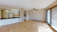 Located at 3185 Karth Rd in White Bear Lake, Minnesota, this single-floor residence offers a practical and comfortable layout with a clean, neutral aesthetic throughout. The open-concept living area is finished with light hardwood-style flooring, a ceiling fan with light fixture, and baseboard heating. Large windows flood the space with natural light and offer views of surrounding greenery, while a sliding glass door provides direct access to an outdoor area. The kitchen is thoughtfully designed with white raised-panel cabinetry, some featuring frosted glass inserts, and light-toned countertops. It is equipped with a full suite of white appliances including an electric range with microwave above, dishwasher, and refrigerator, along with a double stainless steel sink. A pass-through or peninsula connects the kitchen to the main living space, enhancing the open flow. The bedroom features wall-to-wall carpet, a ceiling fan, a wall-mounted AC unit, a baseboard heater, and a window with natural light. The full bathroom includes a vanity with a speckled countertop, a large mirror, towel bars, and a tub and shower combination with white tile surround. Overall, the space presents a functional and well-maintained interior suited for comfortable everyday living.