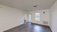 This single-floor unit offers a practical and comfortable layout with three bedrooms, three full bathrooms, and a dedicated kitchen, living room, hallway, and three closets. Throughout the space, durable wood-style flooring in a warm gray-brown tone lends a cohesive, modern look to every room.

The living area is bright and open, featuring large windows with blinds that allow natural light to fill the space. A glass-paneled front door adds additional daylight and provides views of the surrounding outdoor area, which includes green lawn space and a picnic area. A second entry door connects to adjacent rooms, enhancing the flow of the layout.

The kitchen is well-appointed with white cabinetry, ample counter space, a stainless steel sink, and a white electric range with overhead ventilation. Track lighting above the kitchen adds functional illumination, and a pass-through window connects to the adjacent space.

Each bedroom is comfortably sized, with ceiling fans providing year-round climate control. The bedrooms feature neutral walls, wood-style flooring, and windows that bring in natural light. The primary bedroom offers a generous footprint with its own closet. The three bathrooms are clean and functional, each featuring a tub-shower combination with white tile surround, a vanity with storage cabinetry, and matching wood-style flooring.