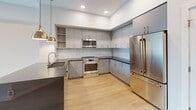 This contemporary 660 square foot apartment in Salt Lake City offers a blend of style and functionality. The single-level layout encompasses one bedroom, one bathroom, and an array of modern amenities. The primary bedroom, measuring 130 square feet, provides ample space and includes access to a private balcony, offering an outdoor extension to the living area.

The kitchen is a highlight, featuring sleek cabinetry with a two-tone design of light grey upper cabinets and white lower cabinets. High-end stainless steel appliances, including a French door refrigerator and built-in microwave, complement the space. The kitchen's L-shaped design maximizes efficiency, while a glossy backsplash and contrasting dark countertops add a touch of sophistication.

The bathroom continues the modern aesthetic with a floating vanity, large mirror, and a combination tub-shower with elegant gold fixtures. Light wood-look flooring runs throughout the apartment, creating a cohesive and warm ambiance. The neutral color palette, predominantly in shades of white and light grey, enhances the sense of spaciousness and allows for personal decorating touches.

Additional features include a hallway for improved flow, a closet for storage, and recessed lighting throughout. The apartment's design prioritizes both style and functionality, making efficient use of the 660 square feet to create a comfortable and contemporary living space.
