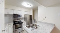 This fully renovated 2-bedroom, 2-bathroom residence offers a thoughtfully updated interior with a clean, modern aesthetic throughout its single-floor layout. The open-concept living area is anchored by a classic fireplace and features durable wood-look plank flooring, a ceiling fan, and multiple windows that invite generous natural light and outdoor views. The updated kitchen is well-appointed with stainless steel appliances — including a refrigerator, range, and over-the-range microwave — complemented by crisp white shaker cabinetry, light granite-style countertops, a double stainless steel sink, and a tile backsplash. A peninsula provides additional prep space and casual seating. Both bedrooms are carpeted for comfort, with large windows offering outdoor greenery views; one bedroom features a sliding glass door for private outdoor access. Each bathroom has been refreshed with wood-look tile flooring, granite-topped vanities, and a full tub-shower combination. Additional highlights include a dedicated laundry area, ample closet and pantry storage, and a consistent neutral color palette that enhances the bright, open feel of the space throughout.