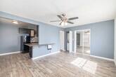 Located at 6635 Crenshaw Blvd in Los Angeles, CA, this efficient single-floor unit offers a thoughtfully designed layout comprising a living room, kitchen, and full bathroom. Light wood-look flooring runs throughout, lending a clean and cohesive aesthetic to the entire space.

The living room is bright and welcoming, featuring multiple windows with slatted blinds that allow generous natural light to filter in. A ceiling fan with integrated lighting provides both comfort and illumination. The room connects seamlessly to the kitchen via a peninsula with a granite countertop overhang — ideal as a breakfast bar or casual dining area.

The kitchen is galley-style and well-equipped, showcasing rich dark wood cabinetry, granite countertops, and a textured mosaic tile backsplash. Black appliances, including a gas range and refrigerator, complete the functional cooking space. Ample upper and lower cabinetry provides considerable storage.

The bathroom is finished with large-format stone-look wall tiles and features a tub-and-shower combination enclosed by sleek frameless sliding glass doors, accented with a decorative mosaic tile border. A sliding mirrored closet door in the main living area adds depth and practicality. The overall palette of soft blue-gray and white tones creates a calm, modern atmosphere throughout.