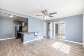 Located at 6635 Crenshaw Blvd in Los Angeles, CA, this efficient single-floor unit offers a thoughtfully designed layout comprising a living room, kitchen, and full bathroom. Light wood-look flooring runs throughout, lending a clean and cohesive aesthetic to the entire space.

The living room is bright and welcoming, featuring multiple windows with slatted blinds that allow generous natural light to filter in. A ceiling fan with integrated lighting provides both comfort and illumination. The room connects seamlessly to the kitchen via a peninsula with a granite countertop overhang — ideal as a breakfast bar or casual dining area.

The kitchen is galley-style and well-equipped, showcasing rich dark wood cabinetry, granite countertops, and a textured mosaic tile backsplash. Black appliances, including a gas range and refrigerator, complete the functional cooking space. Ample upper and lower cabinetry provides considerable storage.

The bathroom is finished with large-format stone-look wall tiles and features a tub-and-shower combination enclosed by sleek frameless sliding glass doors, accented with a decorative mosaic tile border. A sliding mirrored closet door in the main living area adds depth and practicality. The overall palette of soft blue-gray and white tones creates a calm, modern atmosphere throughout.