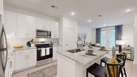 Located at 550 Webb Gin House Rd in Lawrenceville, GA, this single-floor residence offers a thoughtfully designed open-concept layout that seamlessly connects the kitchen, dining, and living areas. The kitchen is a standout feature, showcasing crisp white shaker cabinetry, granite countertops, stainless steel appliances including a range, microwave, and refrigerator, and a central island with a sink and bar seating — ideal for both cooking and casual dining. Light wood-tone flooring runs throughout the main living areas, complementing the bright, neutral color palette.

The living room is bathed in natural light through large windows dressed with floor-to-ceiling drapes, creating an inviting and airy atmosphere. A flexible secondary room provides space for a home office or sitting area. The primary bedroom features plush carpeting, large windows, a ceiling fan, and a serene color-accented accent wall. The bathroom is finished with granite vanity countertops, white cabinetry, and a full tub-shower combination, all set on light wood-look flooring. A dedicated laundry room houses a full-size washer and dryer with overhead shelving for added storage convenience.