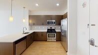 This one-bedroom, one-bathroom residence at 56 Broad Street in Bloomfield, NJ offers a well-designed single-floor layout with modern finishes throughout. The open-concept kitchen is a standout feature, equipped with rich dark-toned cabinetry, a subway tile backsplash, stainless steel appliances including a gas range, over-the-range microwave, dishwasher, and a French door refrigerator. A peninsula with a light quartz countertop and an undermount sink provides additional prep space and is illuminated by stylish pendant lighting, seamlessly connecting the kitchen to the living area. The living and dining space features light hardwood-style flooring that extends throughout the unit, contributing to a bright and cohesive aesthetic. A large window in the bedroom fills the room with natural light, while a wall-mounted HVAC unit ensures year-round comfort. The bathroom is finished with clean white subway tile surrounding the soaking tub and shower combination, complemented by neutral floor tiles and a warm wood-toned wall cabinet for storage. Recessed lighting and a louvered closet door add thoughtful functional details to this well-appointed home.