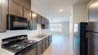 Located at 450 Leclaire St in Davenport, Iowa, this single-floor unit offers a thoughtfully designed layout that maximizes every square foot. The open-concept kitchen flows seamlessly into the living area, creating a connected and functional living space. The kitchen is well-appointed with rich dark-stained cabinetry, granite-look countertops, a stainless steel double-basin sink, and black appliances including an electric range, over-the-range microwave, and dishwasher — all finished with light wood-look plank flooring that runs throughout the unit. The living room is bright and airy, featuring a ceiling fan with light fixture and a multi-pane window that invites natural light and views of the surrounding neighborhood. Neutral gray walls and clean white trim create a modern, versatile aesthetic. The bathroom includes tile flooring, a vanity with sink, toilet, and a separate shower area, complemented by a convenient closet with wire shelving just outside the bathroom entrance. Overall, the unit presents a clean, contemporary design with consistent finishes, offering a comfortable and practical living environment in the heart of Davenport.
