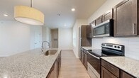 This single-story, 2-bedroom, 2-bathroom home offers a thoughtfully designed layout with modern finishes throughout. Light wood-look flooring flows consistently across all rooms, complemented by neutral warm-beige walls and recessed lighting that create a clean, cohesive aesthetic.

The kitchen is a standout feature, centering around a large granite-topped island with an undermount sink and pendant lighting. Dark espresso cabinetry provides generous storage, while stainless steel appliances—including a refrigerator, electric range, built-in microwave, and dishwasher—complete the space. A white subway tile backsplash adds a classic touch.

The living room is bright and open, with a triple window arrangement that allows ample natural light. The spacious primary bedroom includes a ceiling fan and a dedicated window, offering comfortable airflow and light. Both bedrooms feature panel-style doors and access to closet space. The bathrooms are well-equipped, featuring granite-topped vanities with dark cabinetry and tiled tub-shower combinations.

A dedicated laundry room houses a full-size washer and dryer with overhead wire shelving for added convenience. The entrance includes staircase access and a window for natural light. Overall, the home presents a clean, move-in-ready environment with functional and attractive design details throughout.