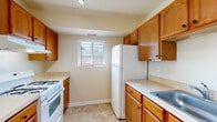 This single-floor residence offers a functional and comfortable layout designed for everyday living. The entry opens into a spacious living area finished with plush wall-to-wall carpeting and a ceiling fan, creating a relaxed and airy atmosphere. A large window with horizontal blinds allows natural light to fill the room, while a tiled entryway provides a practical transition from outside.

The kitchen is well-appointed with warm oak cabinetry spanning both upper and lower sections, offering generous storage throughout. Light-toned countertops provide ample prep space, complemented by white appliances including a gas range, refrigerator, and dishwasher. The kitchen is accessible from the living area via a peninsula counter, creating a semi-open feel. Tile flooring and a window above the counter complete the space.

The bedrooms are carpeted and bathed in natural light from sizable windows, each offering a calm and private retreat with closet access. The neutral beige walls throughout the home contribute to a bright and cohesive aesthetic.

The bathroom features a full-size soaking tub with a clean white surround, alongside a private water closet. An electrical panel is conveniently located in the hallway connecting the main living spaces to the bedrooms, adding to the home's practical design.