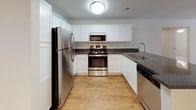 This renovated 3-bedroom, 2-bathroom single-floor residence offers a well-designed layout that balances functional living spaces with updated finishes throughout. The kitchen serves as a central highlight, featuring white shaker-style cabinetry, dark granite-style countertops, and a full suite of stainless steel appliances including a refrigerator, range, microwave, and dishwasher. A peninsula counter extends the workspace while creating a natural transition into the open living and dining area, which is finished with warm wood-style flooring and track lighting overhead.

The living area flows seamlessly from the kitchen, providing a generous and adaptable space suited for a variety of furniture arrangements. Each of the three bedrooms is carpeted for comfort and includes a ceiling fan with light fixture, as well as windows fitted with blinds that allow for natural light and outdoor views. The bedrooms offer ample wall space and a quiet, neutral palette.

The two bathrooms are finished with wood-style flooring, white cabinetry, and granite-style countertops. One bathroom features a tub-shower combination with built-in wire shelving for additional storage, while the second includes a large vanity mirror with Hollywood-style lighting. Together, these details reflect a cohesive and practical renovation throughout the home.