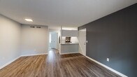 Located at 4901 Randall Pkwy in Wilmington, NC, this single-floor unit offers a clean, modern aesthetic throughout. Rich hardwood-style flooring extends across the open-concept living and dining area, complemented by neutral gray walls and crisp white trim that create a bright, contemporary atmosphere. A bold charcoal accent wall anchors the living space, adding depth and visual interest. A sliding glass door floods the room with natural light and provides outdoor access, offering views of the surrounding greenery.

The kitchen is thoughtfully designed with a peninsula counter finished in light granite, a stainless steel sink with a modern faucet, white cabinetry, and stainless steel appliances including a refrigerator and range. The peninsula layout connects the kitchen to the living area, making the space ideal for both daily living and entertaining.

The bathroom is outfitted with a full tub-shower combination, white cabinetry, brushed gold hardware, and a granite-topped vanity with an undermount sink — all finished with tasteful, durable materials. The overall design of this unit balances functionality with modern style, making it a practical and attractive living space in Wilmington, NC.