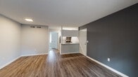 Located at 4901 Randall Pkwy in Wilmington, NC, this single-floor unit offers a clean, modern aesthetic throughout. Rich hardwood-style flooring extends across the open-concept living and dining area, complemented by neutral gray walls and crisp white trim that create a bright, contemporary atmosphere. A bold charcoal accent wall anchors the living space, adding depth and visual interest. A sliding glass door floods the room with natural light and provides outdoor access, offering views of the surrounding greenery.

The kitchen is thoughtfully designed with a peninsula counter finished in light granite, a stainless steel sink with a modern faucet, white cabinetry, and stainless steel appliances including a refrigerator and range. The peninsula layout connects the kitchen to the living area, making the space ideal for both daily living and entertaining.

The bathroom is outfitted with a full tub-shower combination, white cabinetry, brushed gold hardware, and a granite-topped vanity with an undermount sink — all finished with tasteful, durable materials. The overall design of this unit balances functionality with modern style, making it a practical and attractive living space in Wilmington, NC.