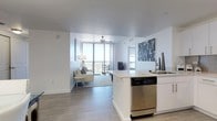 This contemporary single-floor residence is designed with a clean, modern aesthetic throughout, characterized by white walls, light wood-look tile flooring, and an abundance of natural light. The open-concept living and dining area flows seamlessly, with the living room anchored by floor-to-ceiling sliding glass doors that lead to a private balcony offering sweeping panoramic views of the surrounding landscape and skyline. A ceiling fan adds a practical touch to the bright, airy space.

The kitchen is well-equipped with white cabinetry, stainless steel appliances including a range, microwave, refrigerator, and dishwasher, complemented by a mosaic tile backsplash and light stone countertops. The dining area features a pendant light fixture and direct access to the main entry.

Both bedrooms are generously sized, each offering ceiling fans and large windows with expansive outdoor views. A secondary sitting room with floor-to-ceiling glass provides additional flexible living space with equally impressive vistas.

The primary bathroom features a frameless glass-enclosed shower with white subway tile, while the secondary bathroom offers a soaking tub and shower combination. Both bathrooms include white vanities with stone countertops.