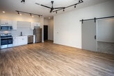 Located at 2004 City Vista Way in Knoxville, Tennessee, this contemporary single-floor residence showcases a thoughtfully designed open-concept layout with clean lines and modern finishes throughout. The expansive living area is anchored by warm light wood flooring, a striking ceiling fan, and a bold track lighting system that provides both ambient and directional illumination. Sliding barn doors add an industrial-chic aesthetic detail while maximizing usable space. Large floor-to-ceiling windows and a sliding glass door open to a private balcony, flooding the interior with natural light and offering views of the surrounding neighborhood. The kitchen is well-appointed with crisp white cabinetry, open shelving, a subway tile backsplash, stainless steel appliances including a range, microwave, dishwasher, and refrigerator, complemented by a matte black faucet. Two carpeted bedrooms each feature ceiling fans, recessed lighting, and windows with exterior views. Two bathrooms mirror the home's modern palette, with white vanities, wood-look flooring, black hardware accents, and one featuring a walk-in shower while the other offers a full bathtub. The overall ambiance is bright, airy, and contemporary.