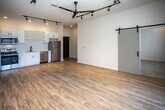 Located at 2004 City Vista Way in Knoxville, Tennessee, this contemporary single-floor residence showcases a thoughtfully designed open-concept layout with clean lines and modern finishes throughout. The expansive living area is anchored by warm light wood flooring, a striking ceiling fan, and a bold track lighting system that provides both ambient and directional illumination. Sliding barn doors add an industrial-chic aesthetic detail while maximizing usable space. Large floor-to-ceiling windows and a sliding glass door open to a private balcony, flooding the interior with natural light and offering views of the surrounding neighborhood. The kitchen is well-appointed with crisp white cabinetry, open shelving, a subway tile backsplash, stainless steel appliances including a range, microwave, dishwasher, and refrigerator, complemented by a matte black faucet. Two carpeted bedrooms each feature ceiling fans, recessed lighting, and windows with exterior views. Two bathrooms mirror the home's modern palette, with white vanities, wood-look flooring, black hardware accents, and one featuring a walk-in shower while the other offers a full bathtub. The overall ambiance is bright, airy, and contemporary.
